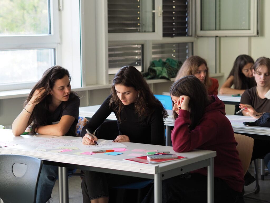 Three young women sitting at a table discussing a collaborative activity