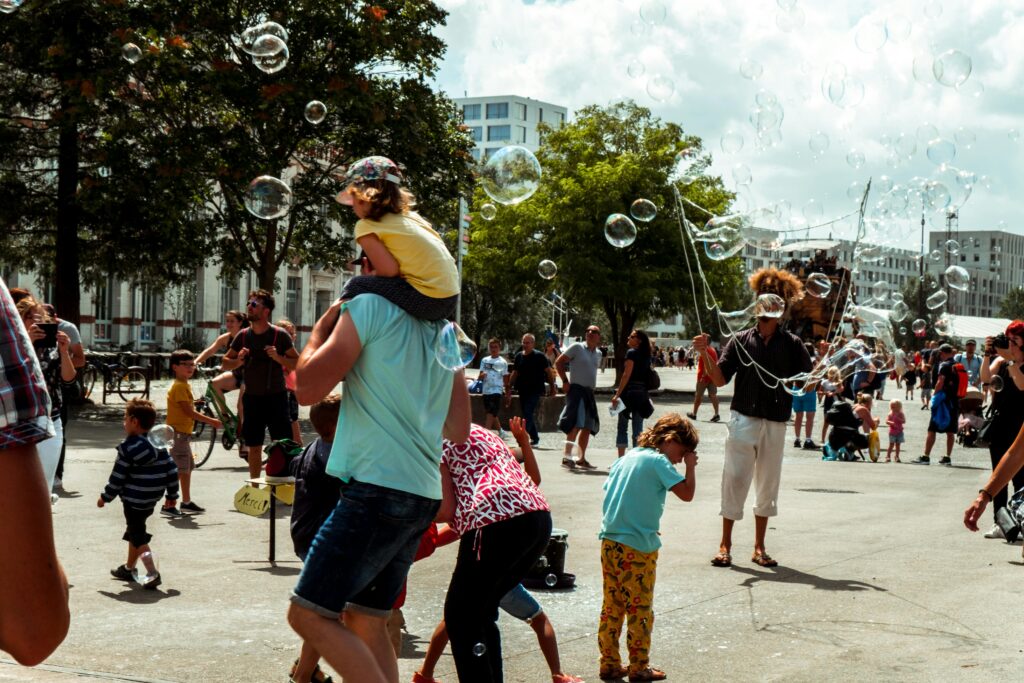 Children and adults on a square in the sunshine while someone blows soap bubbles