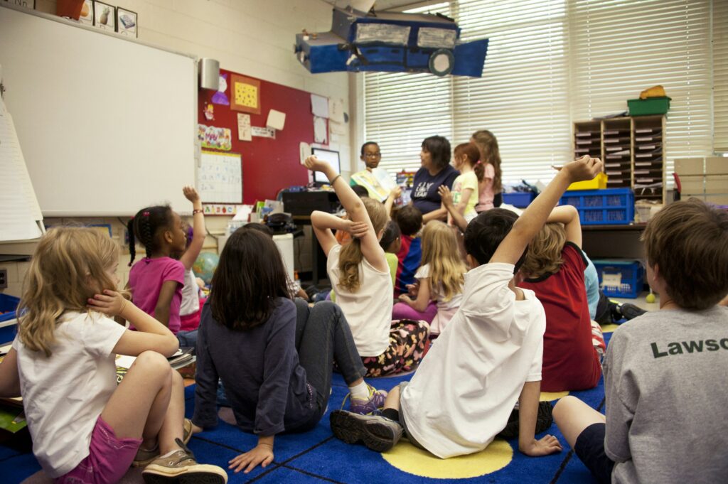 A classroom scene where school children and their teacher are reading a book together.